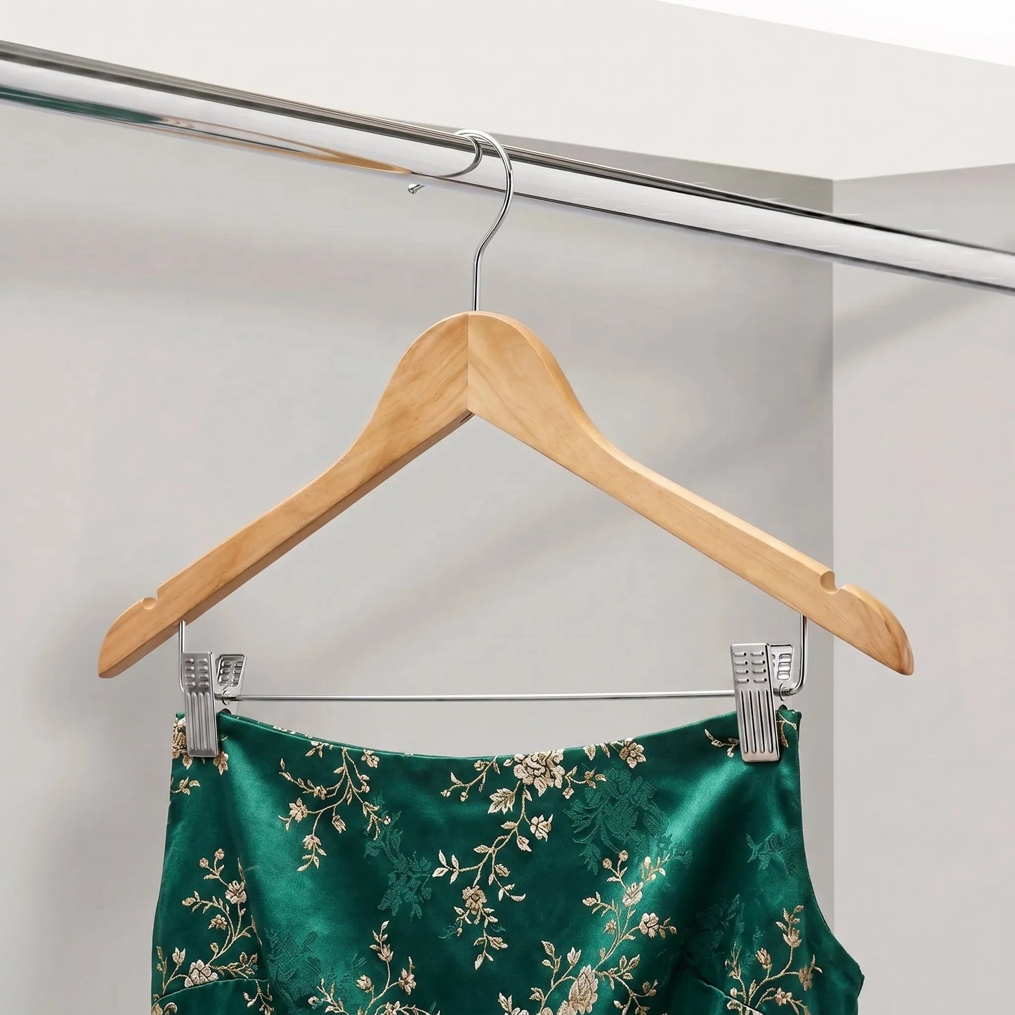 Green satin garment with floral embroidery on a wooden hanger against a white background