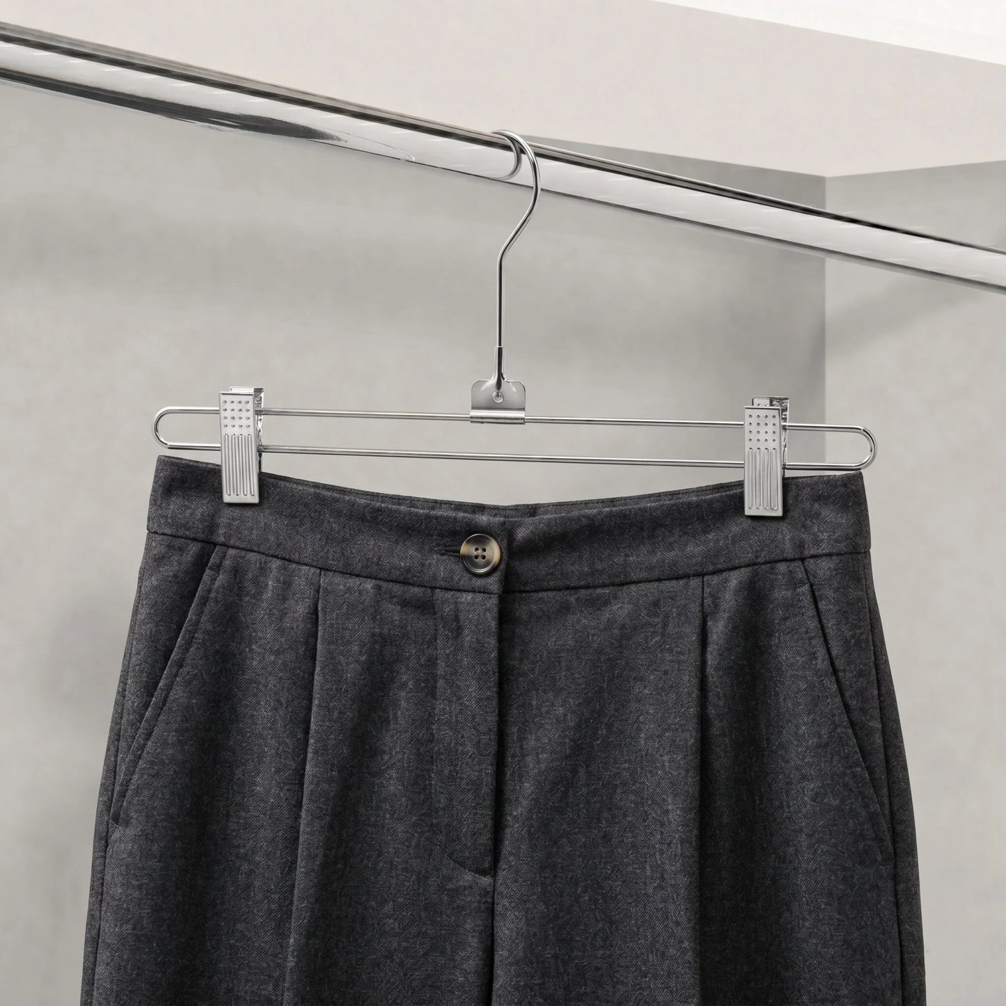 Gray pants hanging on a metal hanger against a neutral background