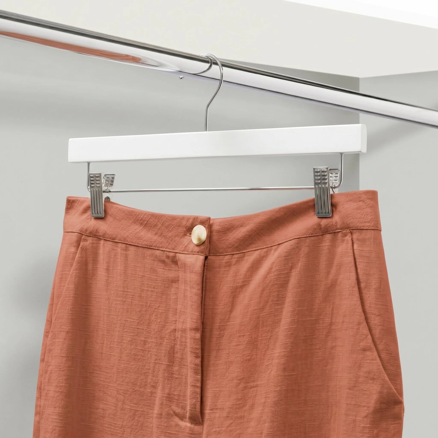 orange trouser hang on a white wood pant hanger inside a wardrobe
