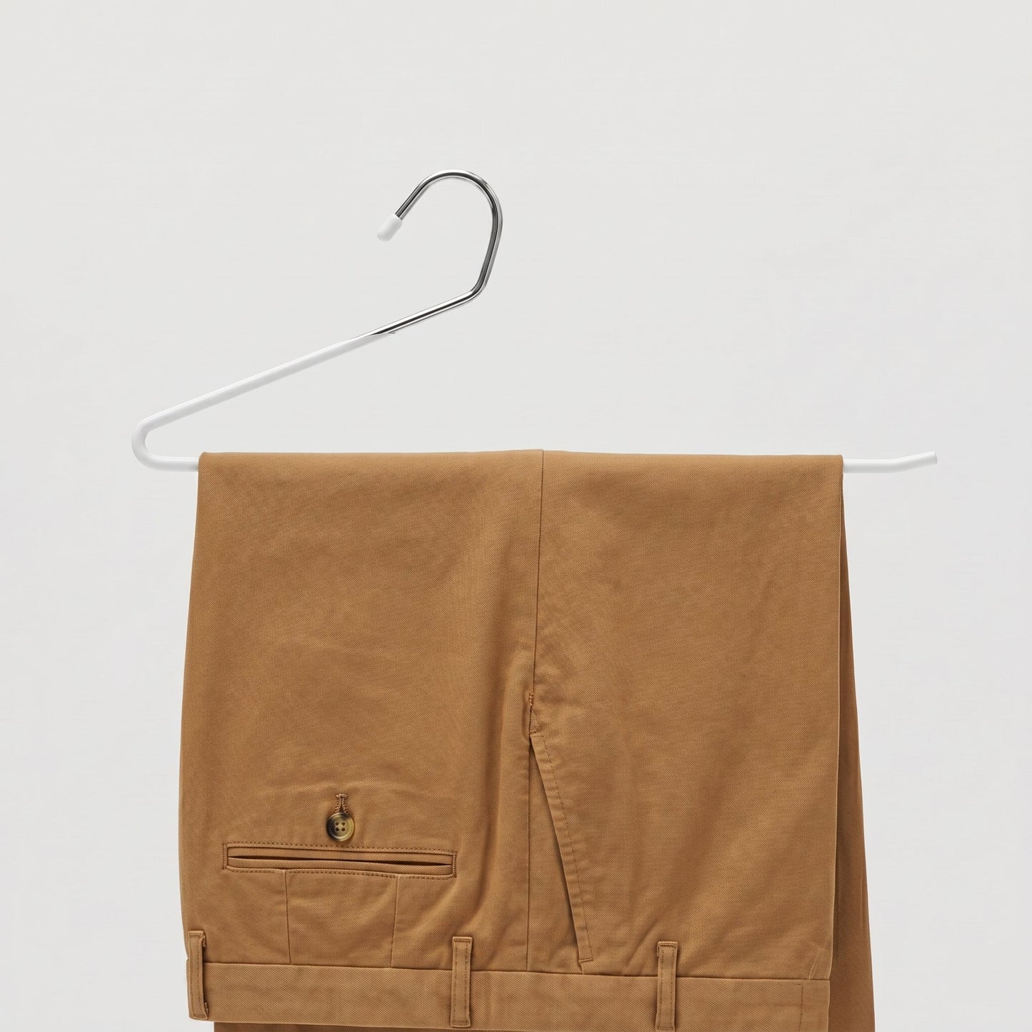 Brown pants hanging on a white hanger against a light gray background